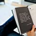 A person incorporates the Men's Gratitude Journal from sonia's-vokalized-kreations into their daily routine, holding it open to a page displaying a motivational quote in white text on a black background.