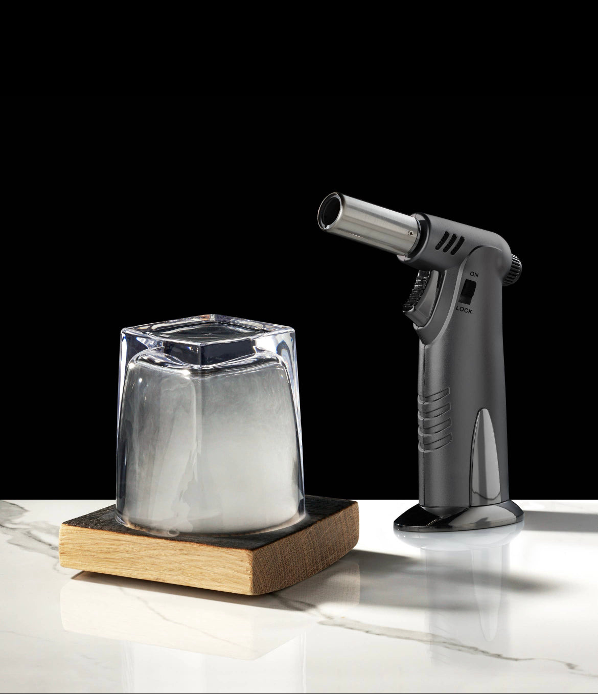 The AlchemI Single Serve Smoked Cocktail Kit by sonia's-vokalized-kreations features a kitchen torch and cocktail smoker with a smoke-filled glass on a wooden square over marble against a black backdrop.
