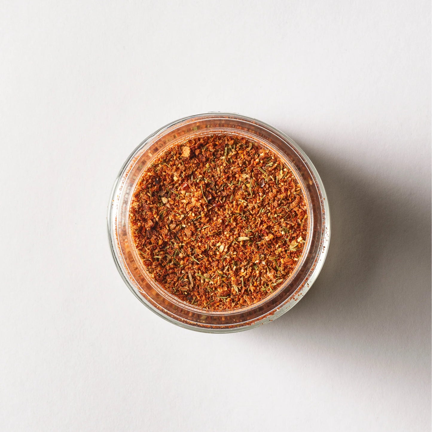 A glass jar containing a vibrant mixed spice blend, similar to a seafood spice mix and displaying red and green flecks on a white surface, is labeled "Seasoned" by Sonia's Vokalized Kreations.
