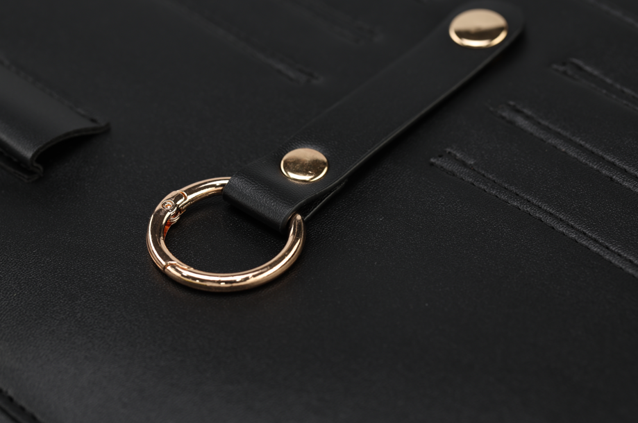 Close-up of a black leather clutch from the Harlem & Brooklyn Bundle by Sonia's Vokalized Kreations, featuring a gold circular ring and button on the strap, with luxurious stitching that embodies the charm of classic black accessories.