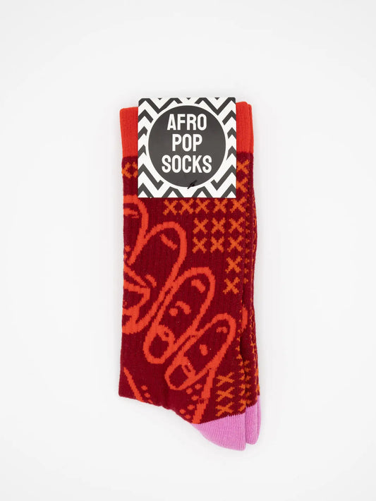 Red and orange BHM Socks by Sonia's Vokalized Kreations feature a bold geometric pattern, made from soft combed cotton, with a black-and-white "Afro Pop Socks" label.