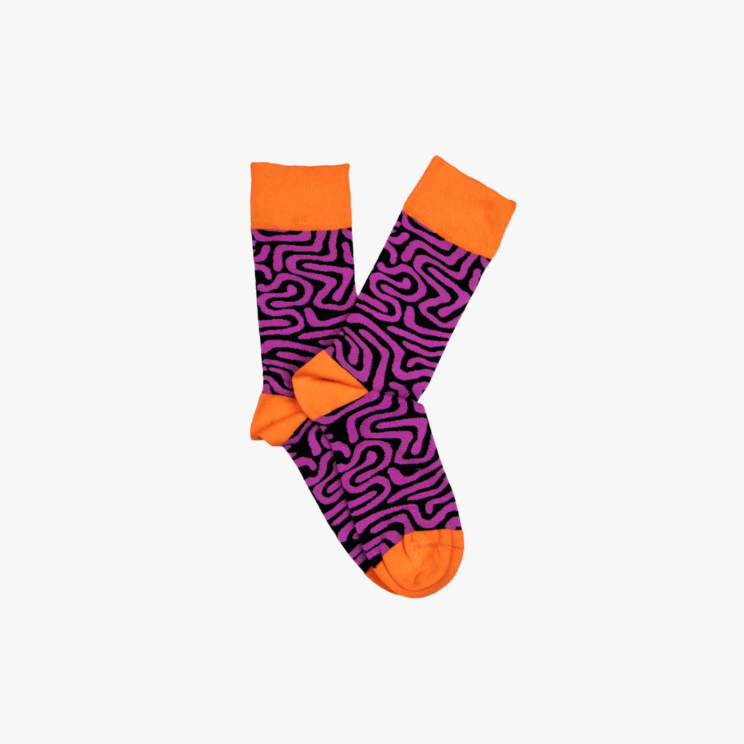 Roots Purple by Sonia's Vokalized Kreations are vibrant socks with an abstract pink and black pattern, accented by bright orange toes, heels, and cuffs.