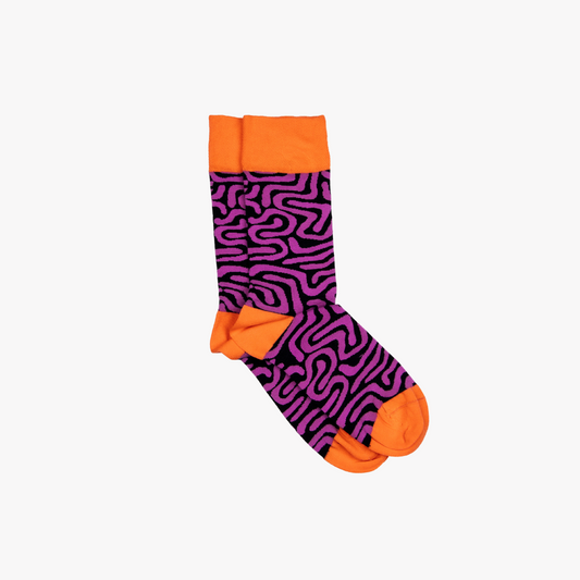 Sonia's Vokalized Kreations' "Roots Purple" socks feature a vibrant purple and black maze design with orange cuffs, heels, and toes, adding an African-inspired pop of color to any plain white background.