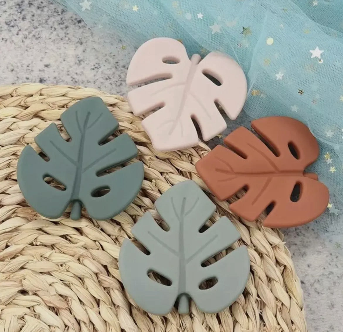 The New Baby Gift Box for Mom & Baby by Sonia's Vokalized Kreations features four leaf-shaped silicone coasters in green, pink, brown, and gray—ideal as a cheerful accent or thoughtful postpartum gift for new parents.