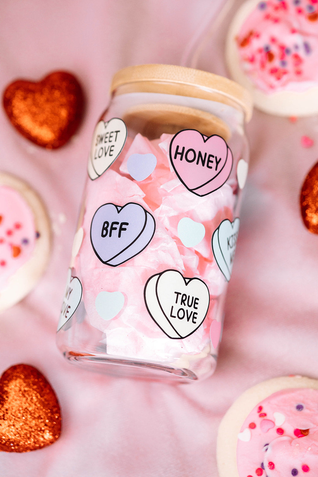 A Libbey Glass Cup by Sonia's Vokalized Kreations, featuring heart-shaped labels with words like "Honey" and "BFF," topped with a bamboo lid, and surrounded by decorated cookies and glittery hearts.