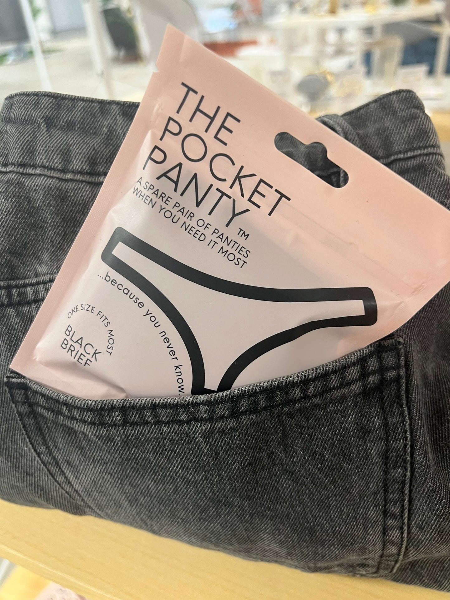 A packet of "The Pocket Panty" by Sonia's Vokalized Kreations is smartly stashed in the back pocket of gray denim pants. The packaging features an illustration of black briefs, subtly ensuring a convenient emergency panty solution.