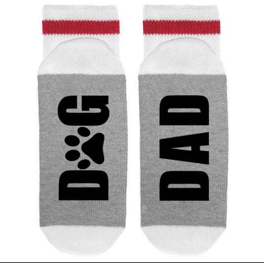 Sonia's Vokalized Kreations' Lumberjack Crew Socks are white and gray mid-calf socks with "DOG" and a paw print on one sock, and "DAD" on the other. These breathable socks offer comfort and style for every dog-loving dad.