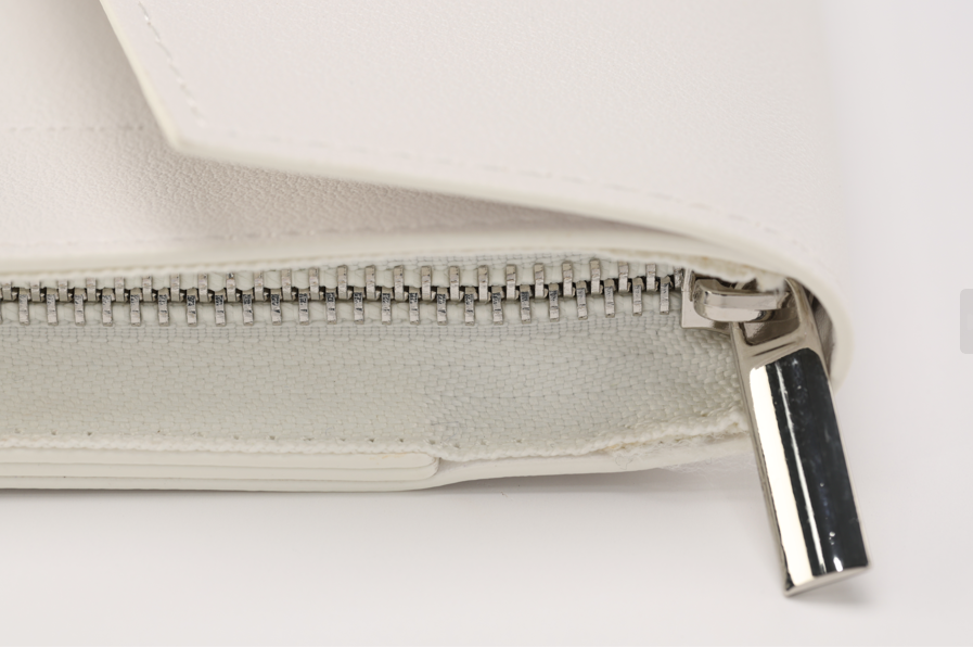 This close-up of Paloma, a white leather wallet from Sonia's Vokalized Kreations, features a metal zipper with a shiny silver pull that adds an elegant touch reminiscent of style icon Paloma.