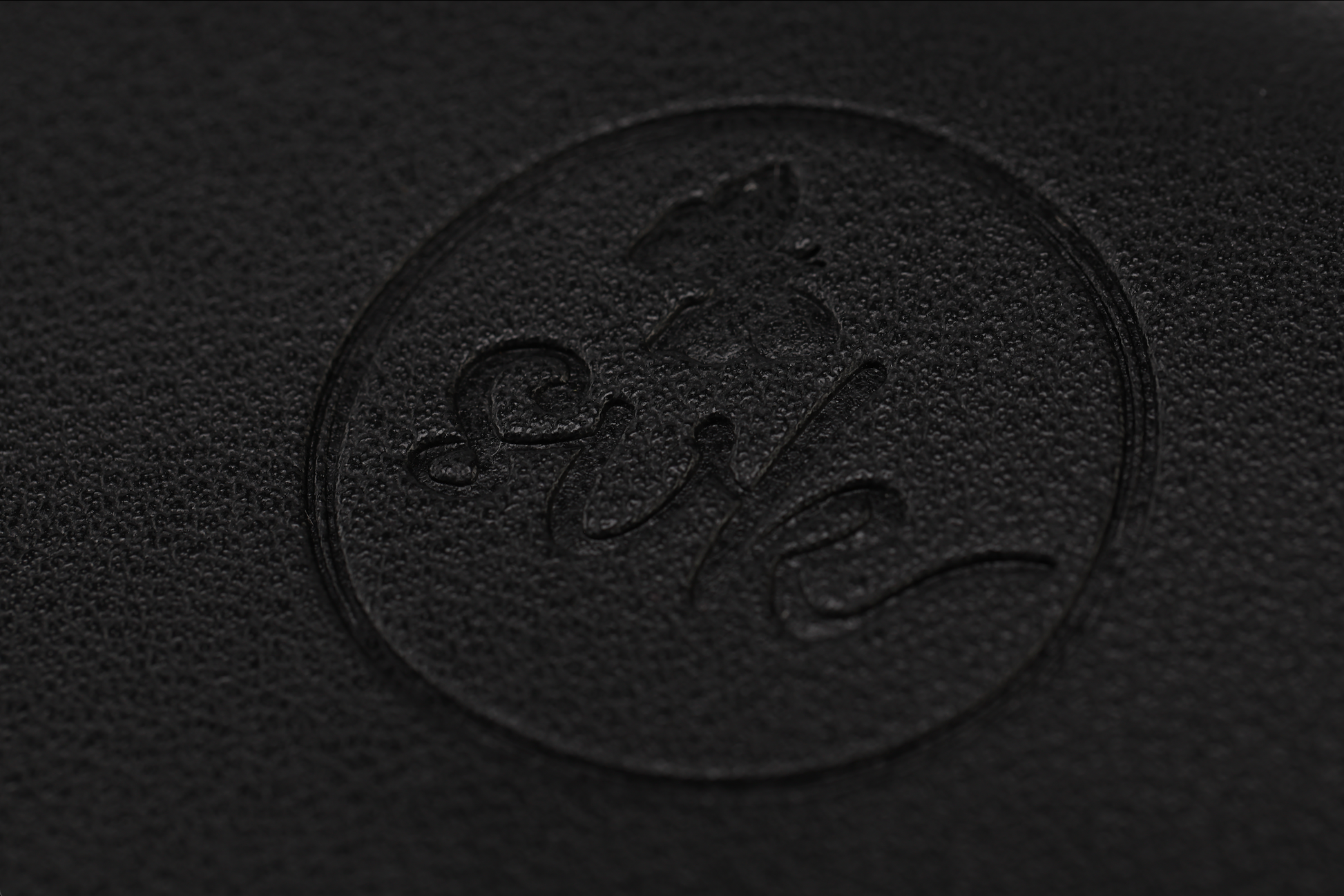 The Harlem Clutch by Sonia's Vokalized Kreations features an embossed black leather finish with a circular stylized logo, embodying timeless elegance.