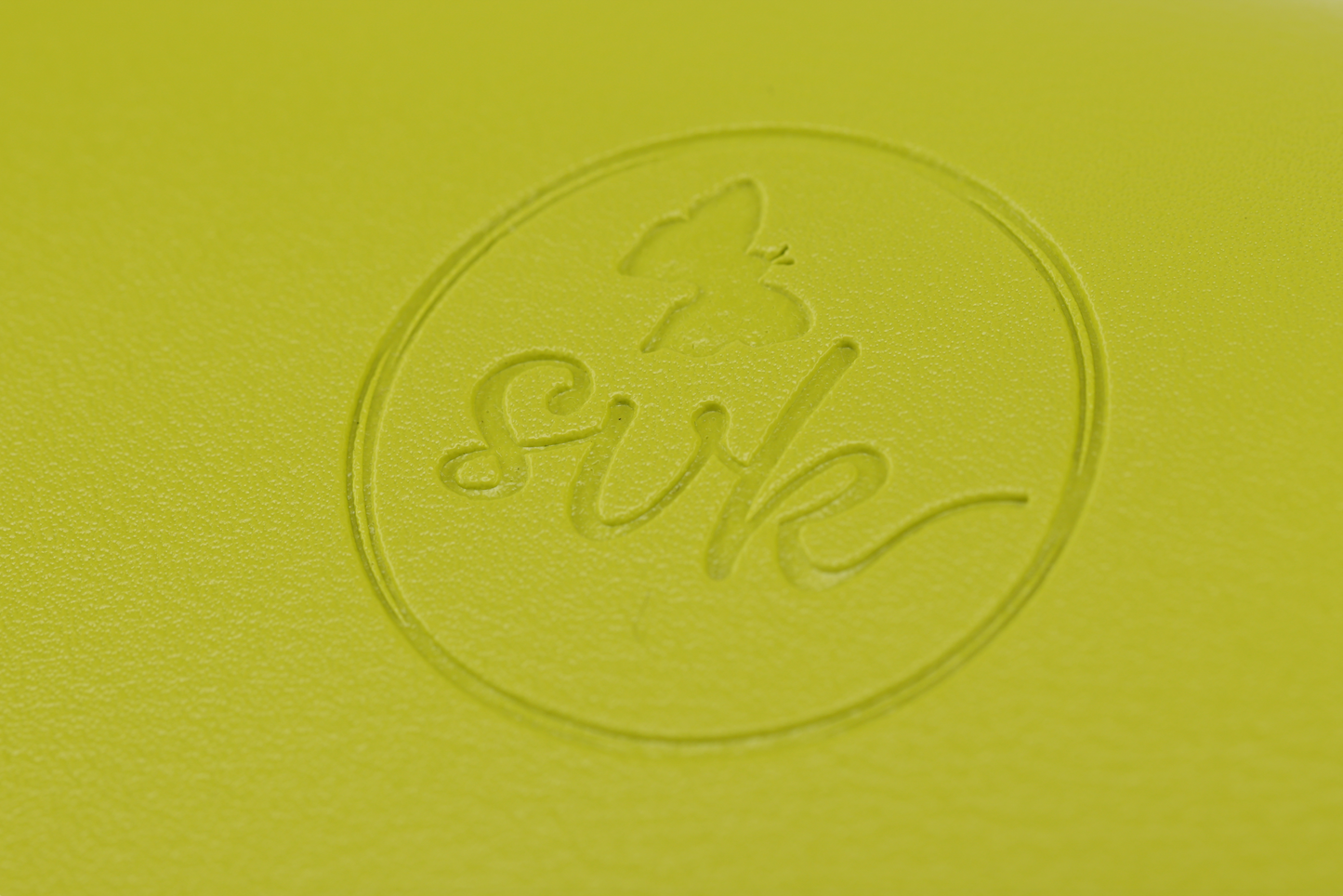 Close-up of a yellow surface featuring Sonia's Vokalized Kreations' embossed butterfly logo and "svk" within a circle, echoing the bold style of the Pompei, empowering women with its striking design.