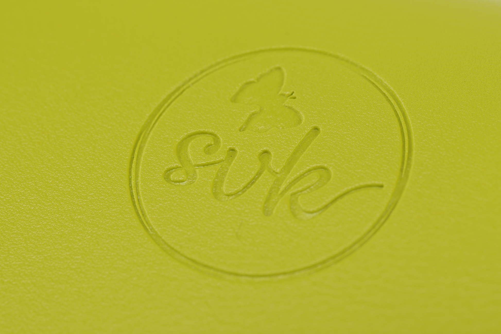 Close-up of a yellow surface featuring Sonia's Vokalized Kreations' embossed butterfly logo and "svk" within a circle, echoing the bold style of the Pompei, empowering women with its striking design.
