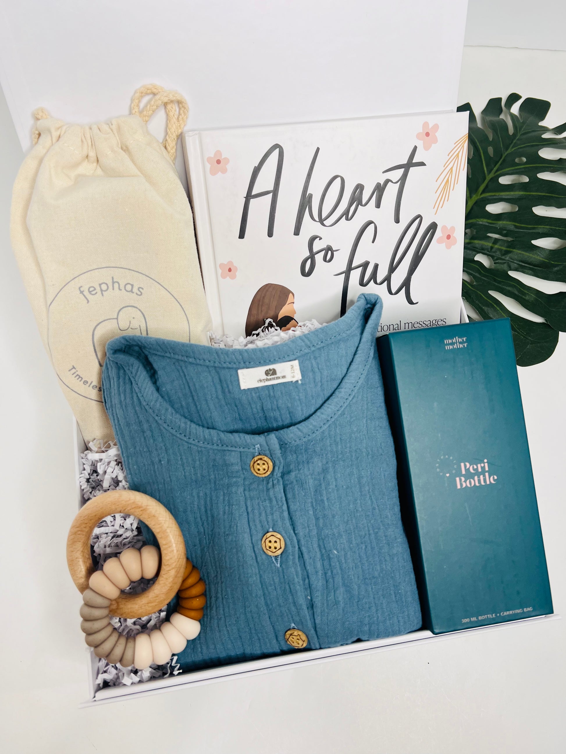 The New Baby Gift Box for Mom & Baby by Sonia's Vokalized Kreations includes a blue buttoned shirt, teal Perl bottle box, wooden teether, drawstring pouch, "A Heart So Full" book, and decorative green leaf—perfect for showers or postpartum care.