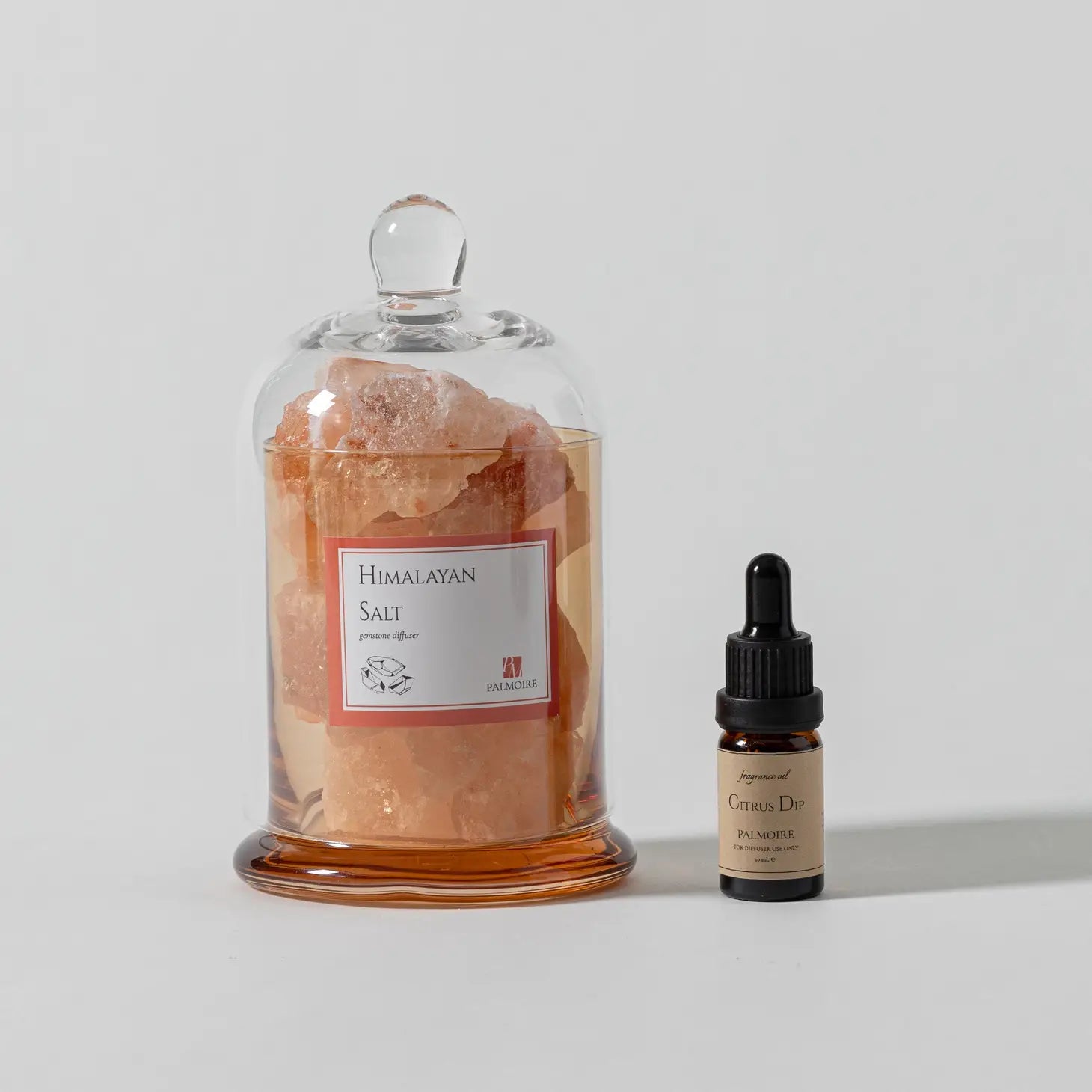 A jar labeled "Himalayan Salt Gemstone Diffuser" from Sonia's Vokalized Kreations sits beside a dropper bottle of "Citrus Dip," evoking the allure of exotic fragrance oils on a plain background.