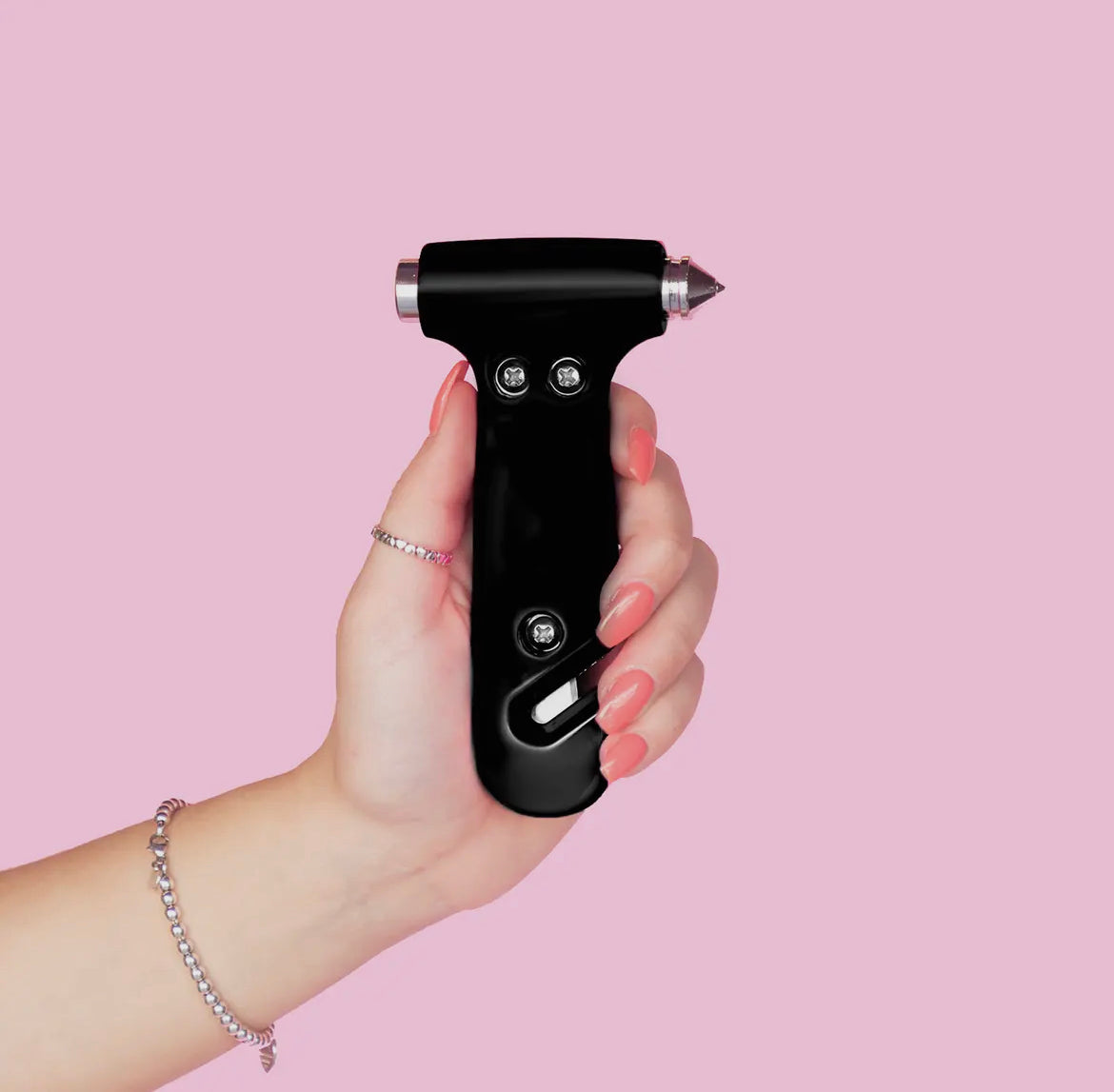 A hand with pink nails holds The Glammer Hammer by Sonia's Vokalized Kreations, featuring a pointed metal tip and black handle, designed as a car escape tool against a pink background.