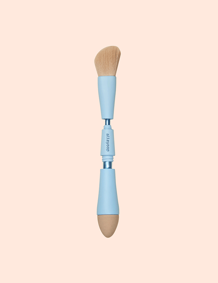 Sonia's Vokalized Kreations' 4 in 1 Makeup Brush is a travel-friendly tool featuring a fluffy angled brush on one end and a rounded sponge applicator on the other, both with light blue handles, perfect for effortless beauty on the go.