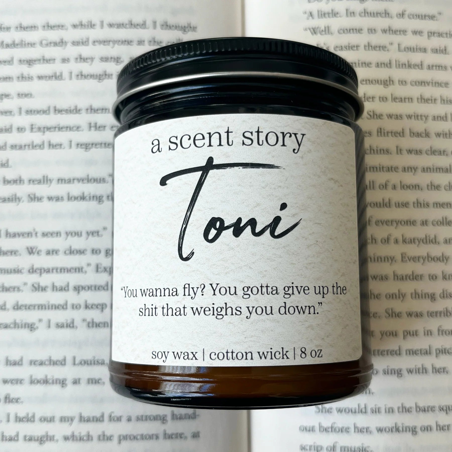 A glass candle jar labeled "Don't Disturb My Peace" from Sonia's Vokalized Kreations rests on an open book, exuding tranquility. The label highlights a quote and details about the soy wax, cotton wick, and size: 8 oz, inviting mindfulness with every flicker.