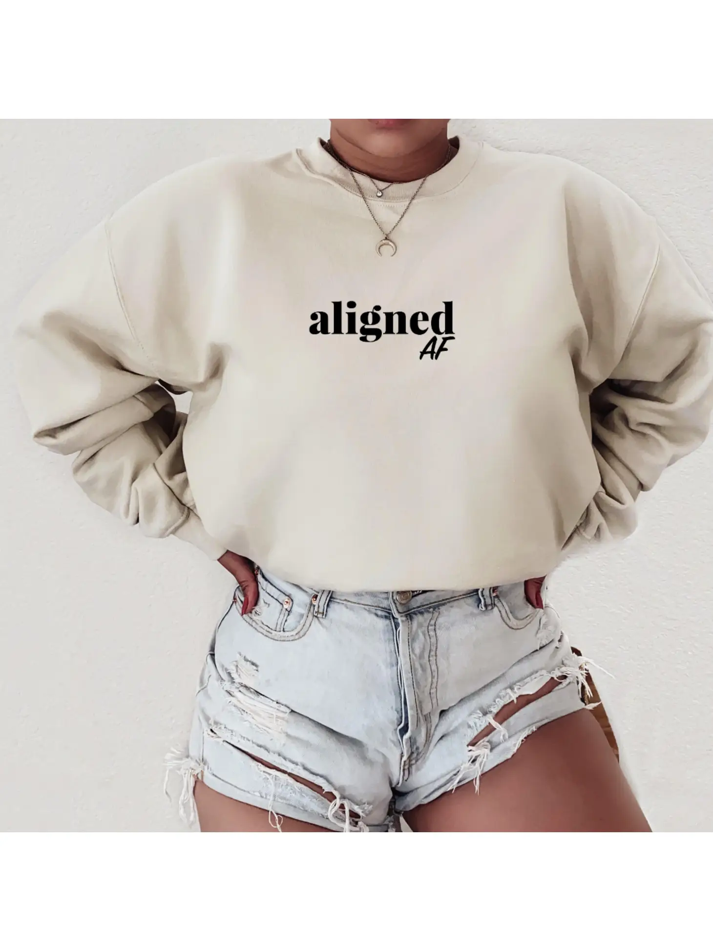 A person exudes tranquility in Sonia's Vokalized Kreations' "Don't Disturb My Peace" beige sweatshirt, featuring "aligned AF" text, and pairs it with light denim shorts.