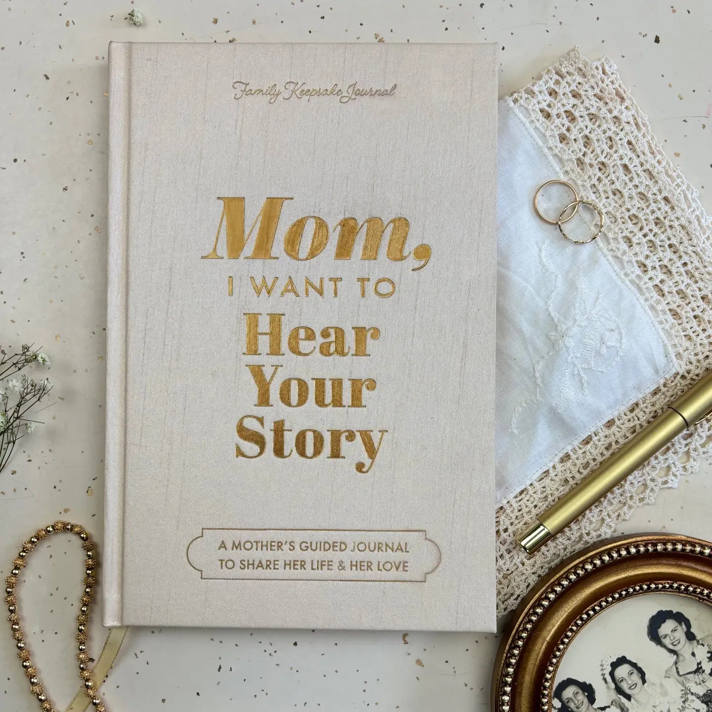 The beige "Mom, I Want To Hear Your Story; Heirloom Edition" journal by Sonia's Vokalized Kreations rests on a table with keepsakes—a thoughtful gift and cherished keepsake for mothers.