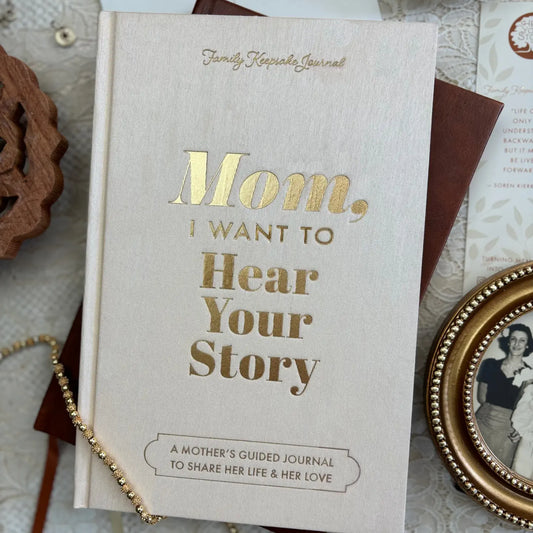 The "Mom, I Want To Hear Your Story; Heirloom Edition" journal by Sonia's Vokalized Kreations rests on lace beside keepsakes—a thoughtful gift for mothers to record and share memories with loved ones.