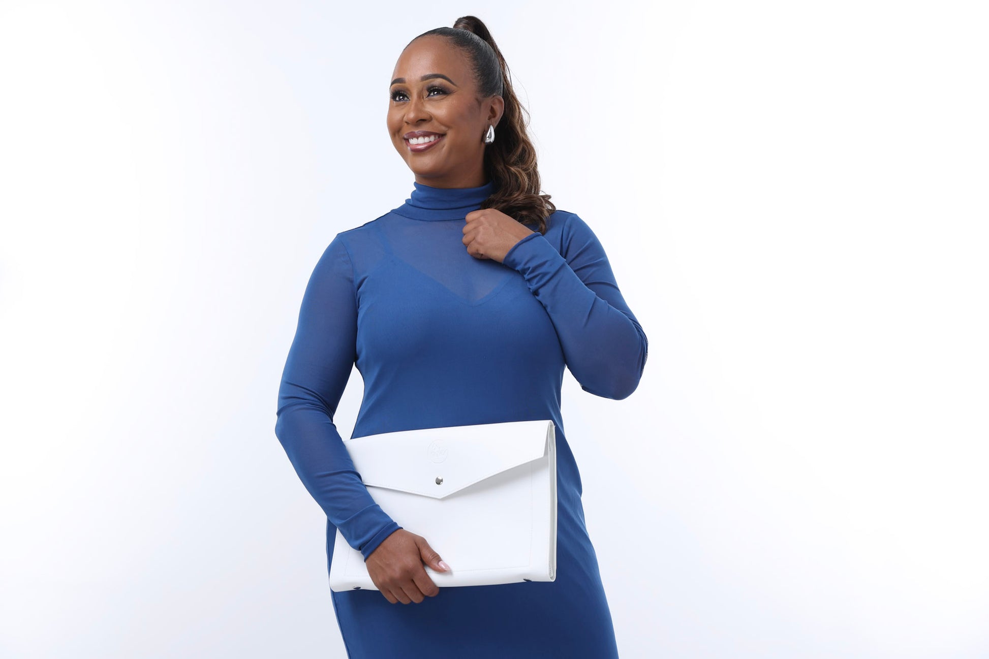 A fearless woman in Sonia's Vokalized Kreations' Paloma blue dress holds a large white envelope, smiling and looking slightly to the right against a plain background.