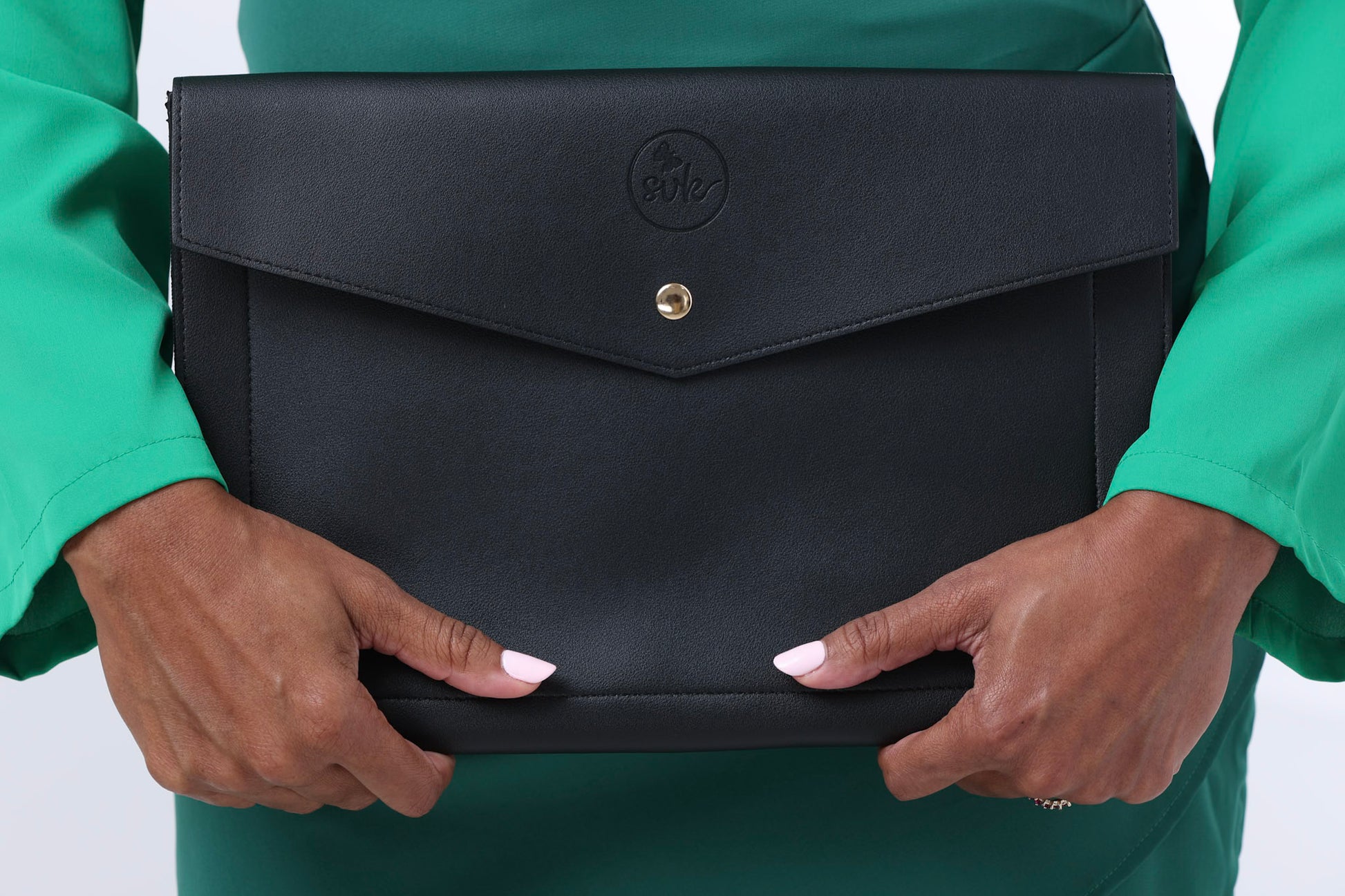 A person in a green top holds Sonia's Vokalized Kreations' Harlem, a black leather clutch with a button closure that exudes timeless elegance.