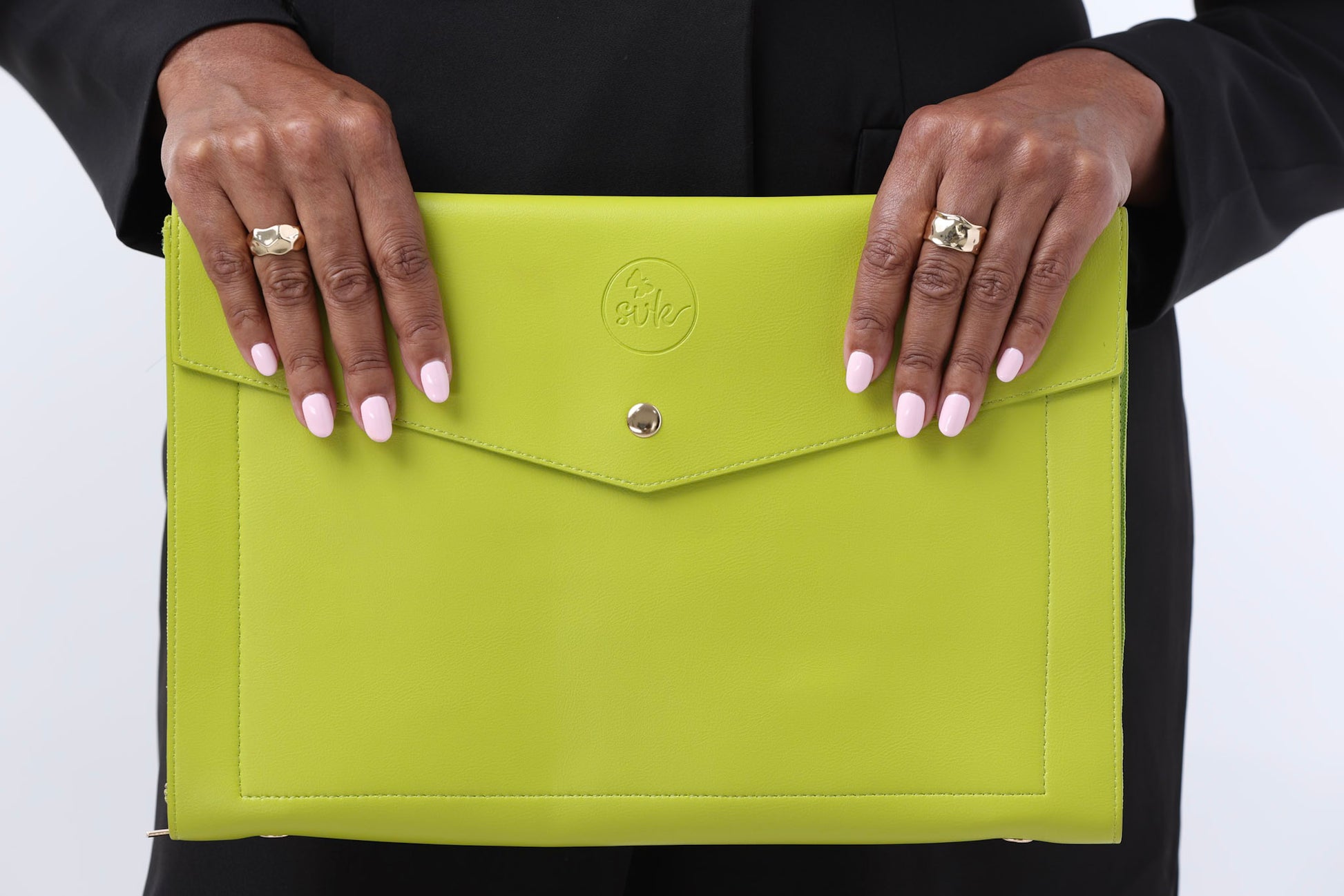Confidently holding a vibrant Pompei clutch by Sonia's Vokalized Kreations, its green hue and circular logo stand out against their sleek black outfit, embracing a bold style that empowers women.