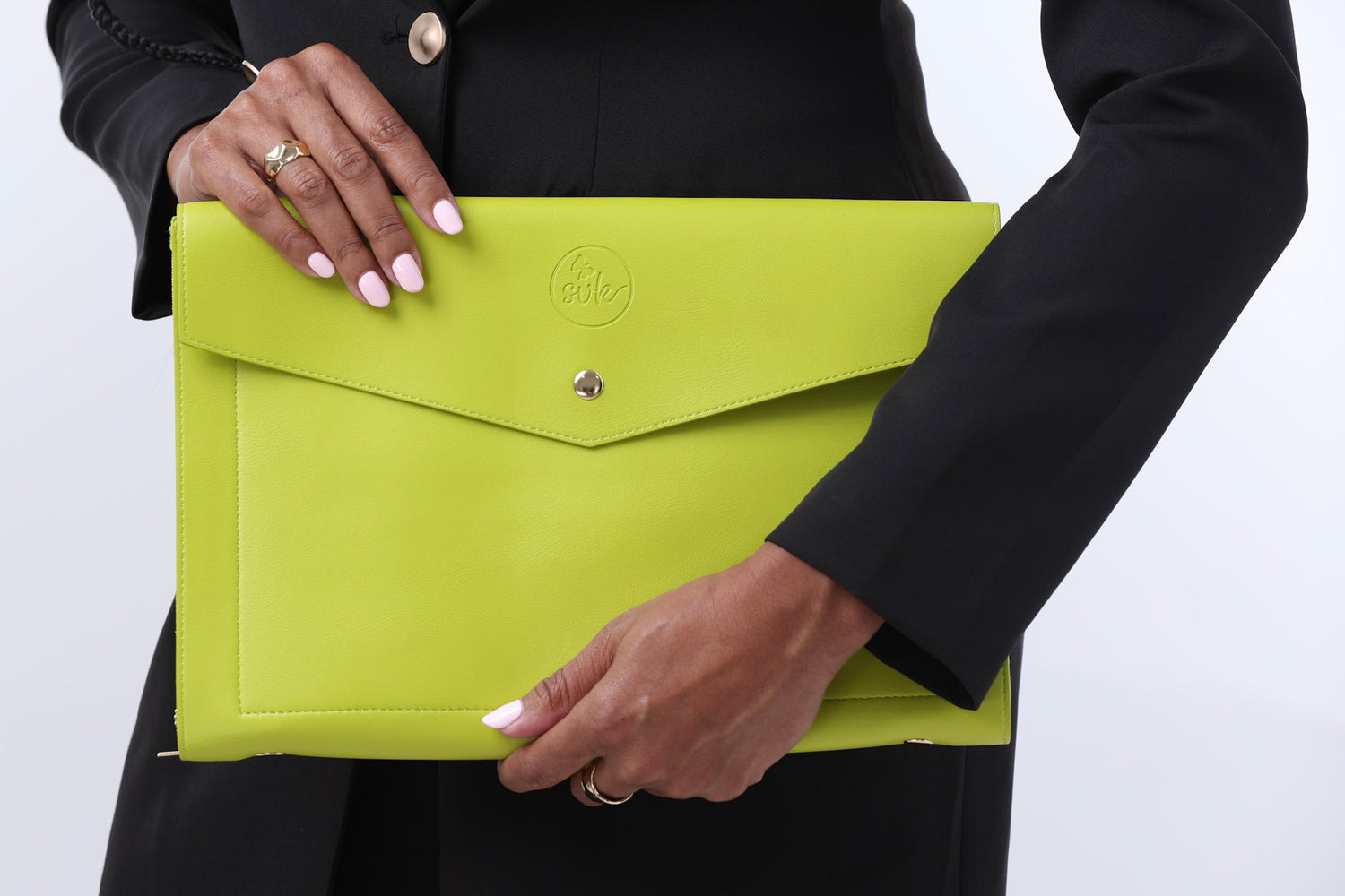 A person in a black outfit displays Sonia's Vokalized Kreations' Pompei Clutch in a vibrant green with button closure, exuding bold style.