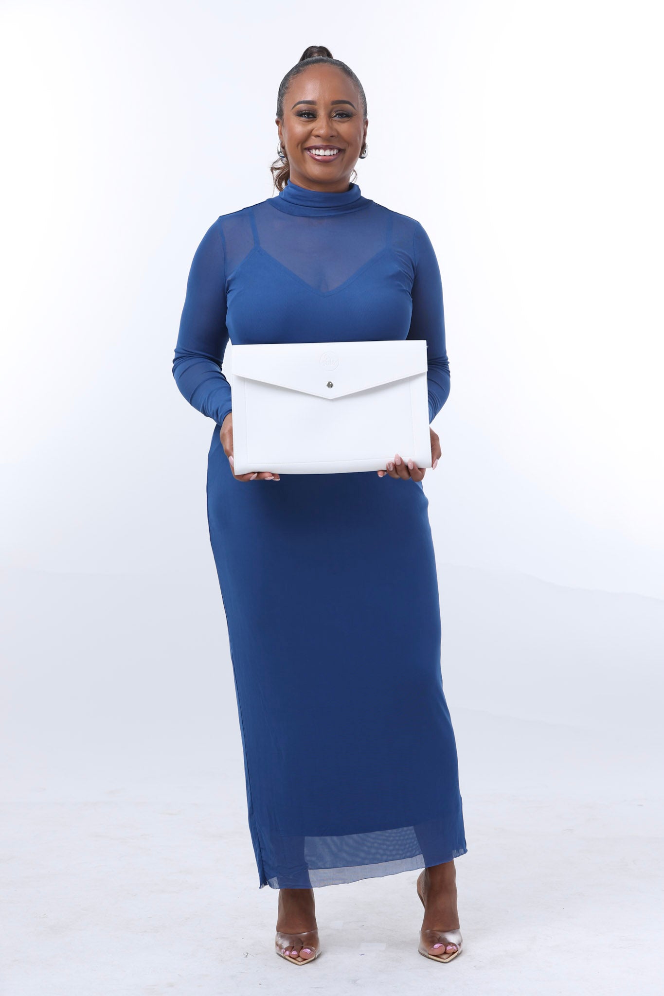 A fearless woman wearing a long blue dress confidently holds a large, white envelope-shaped object against a plain background, embodying Paloma's bold statement style from Sonia's Vokalized Kreations.