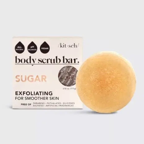 The Sugar Exfoliating Body Scrub Bar by Sonia's Vokalized Kreations is shown beside its packaging. It features clean beauty attributes: all-natural, pH balanced, vegan, and free from parabens, phthalates, silicones, sulfates, and artificial fragrances. Made with nourishing coconut oil for a silky finish.