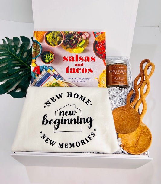 The "Taco ‘Bout a New Beginning” Housewarming Box by Sonia's Vokalized Kreations includes a Salsas & Tacos cookbook, labeled pouch, taco spice blend jar, and wooden utensils—ideal for celebrating a new home.