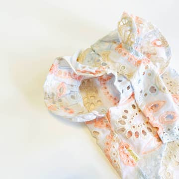 Close-up of the Summer Princess Vintage Style Handmade Pet Dress-Shirt by Sonia's Vokalized Kreations, featuring a light-colored pattern with lace-like cutouts, crafted from breathable fabric, lying unfolded on a white surface.