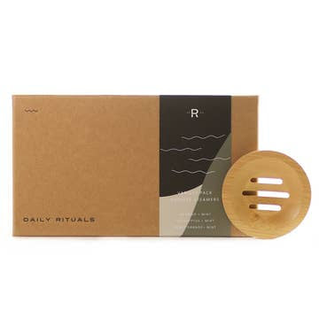 A brown rectangular box labeled "Shower Steamers | Variety Pack" from Sonia's Vokalized Kreations sits beside a round wooden soap dish with slots, providing a spa-like experience for your senses.
