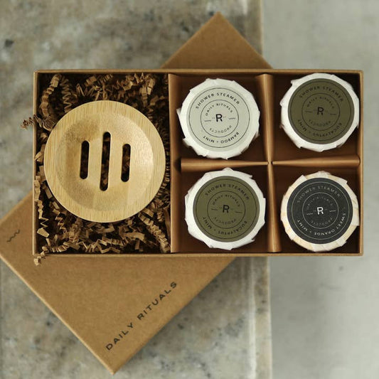 Sonia's Vokalized Kreations offers a "Shower Steamers | Variety Pack" with a spa-like experience featuring four essential oil-infused scents like eucalyptus and mint, neatly arranged under a wooden lid with brown paper filling.