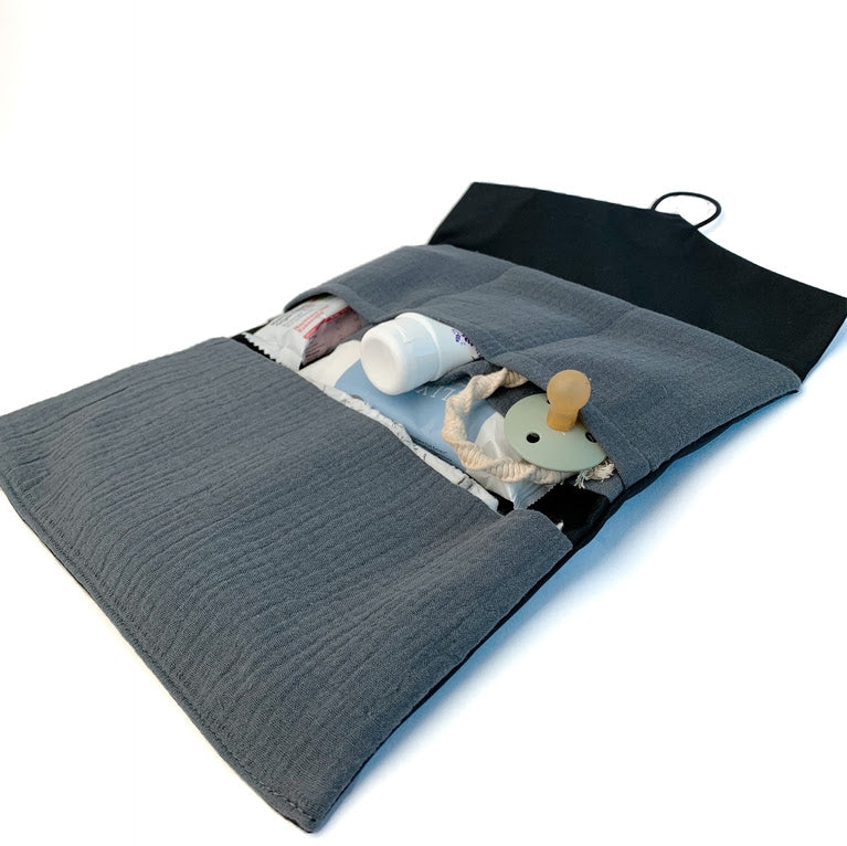 The open gray fabric pouch reveals a Sonia's Vokalized Kreations Diaper Clutch with essentials like a bottle, pacifier, cloth items, and Baby Hair Brush Set—perfect for Mommy, Let's Cuddle! moments.
