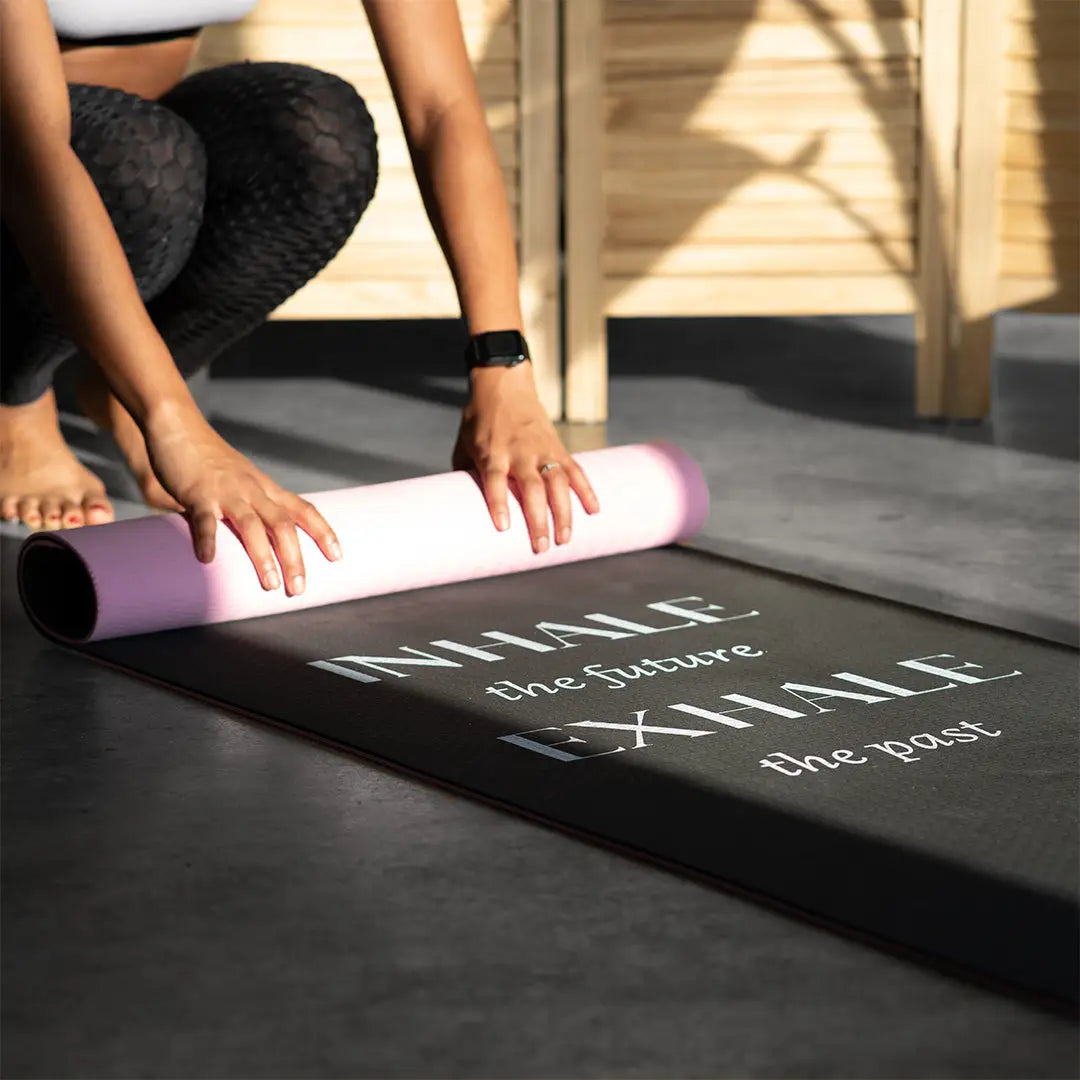 A person in patterned leggings rolls up Sonia's Vokalized Kreations' eco-friendly "Inhale the Future Exhale the Past" yoga mat.