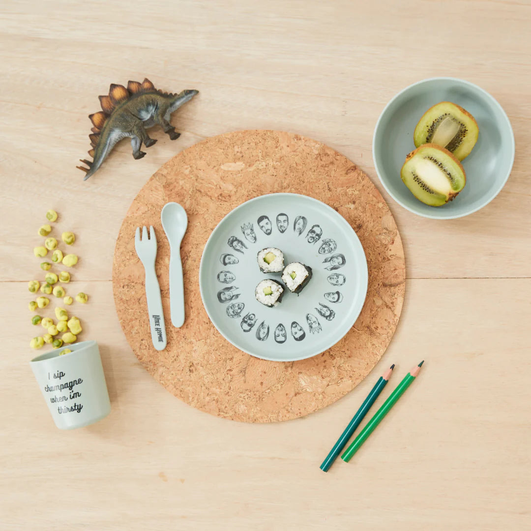 A charming table setting displays a plate of sushi rolls, a dinosaur figurine, kiwi slices in a bowl, and corn kernels—all elegantly arranged on the Baby Bamboo Dinnerware Set by sonia's-vokalized-kreations. Accompanying this is a text cup, cutlery, and colored pencils on a cork mat.