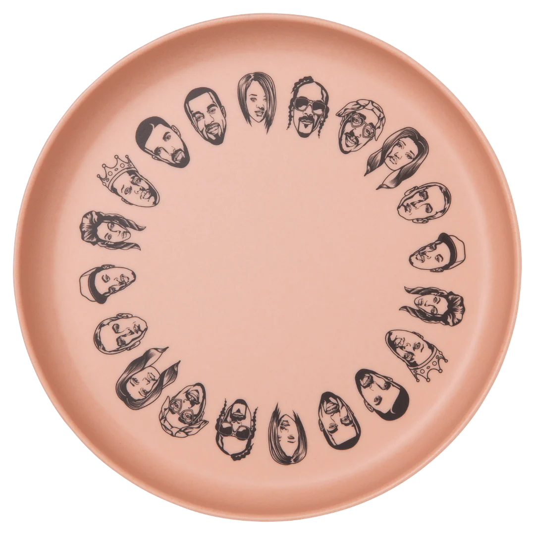 The Baby Bamboo Dinnerware Set by Sonia's Vokalized Kreations features a pink plate adorned with black, cartoon-style faces around the rim, made from eco-friendly bamboo.
