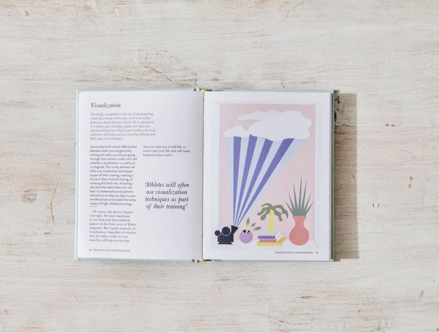 The book "Manifesting For Beginners" by Victoria Jackson from sonia's-vokalized-kreations lies open on a wooden surface, showing text on the left page and a geometric art illustration depicting positive energy, plants, and rays on the right page.