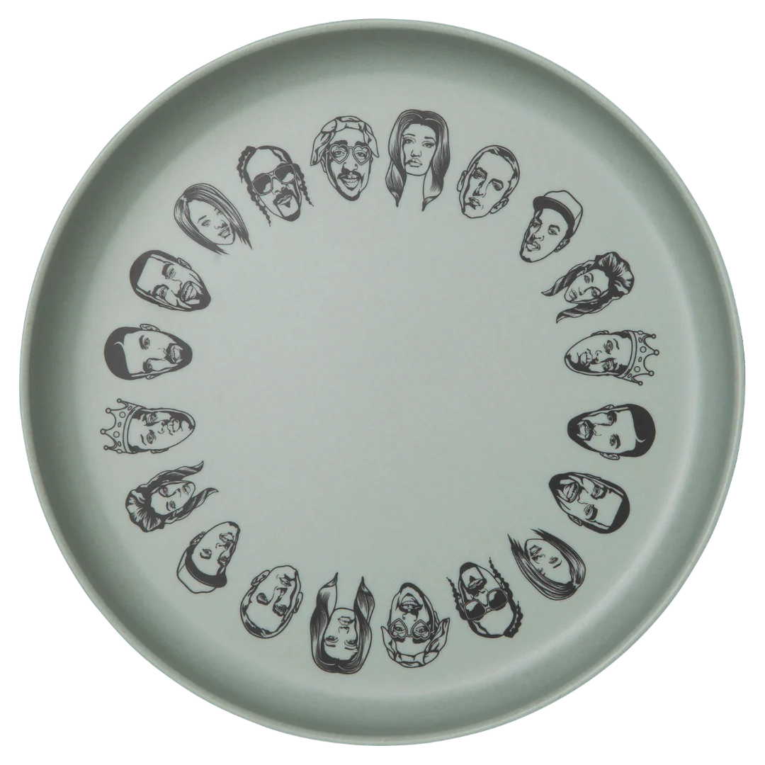 Sonia's Vokalized Kreations offers a round eco-friendly white plate with black hip-hop style illustrations of diverse faces, arranged in a circle, from their Baby Bamboo Dinnerware Set.