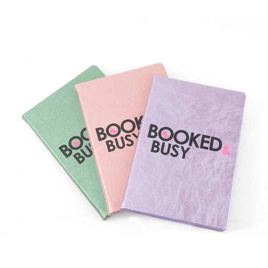 Three "Booked & Busy" journals by sonia's-vokalized-kreations in vibrant green, pink, and purple are arranged overlapping on a white background, ideal for enhancing your organizational routine.