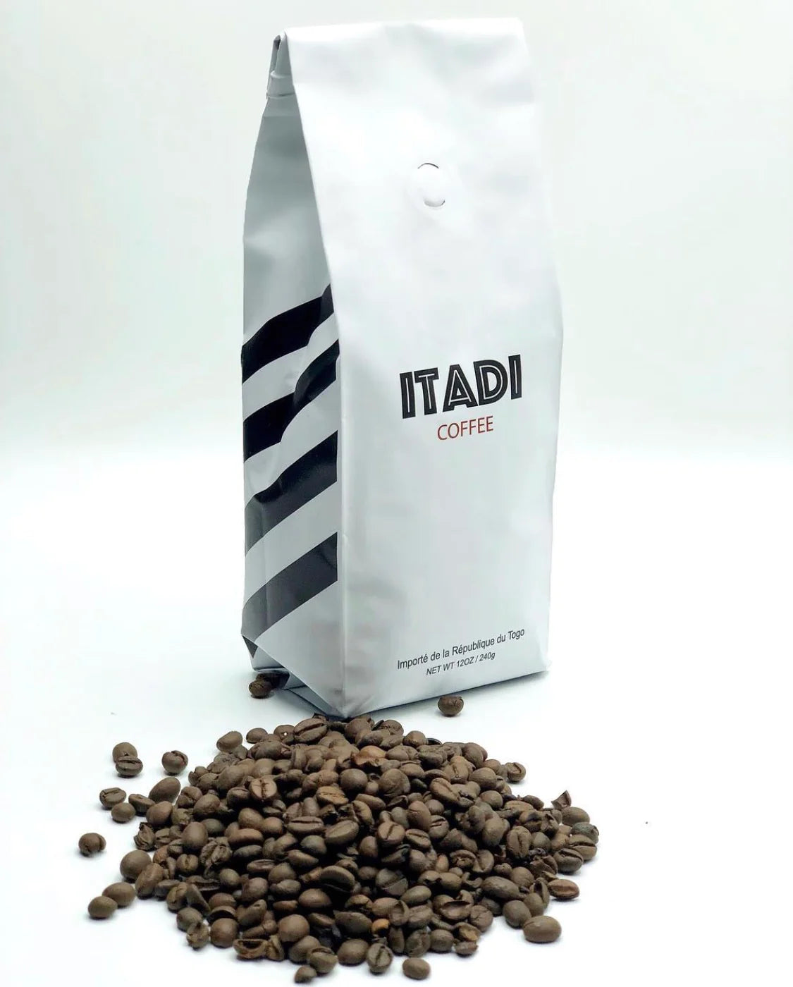 A white bag labeled "Itadi Coffee" by Sonia's Vokalized Kreations, with a pile of robusta coffee beans on a white backdrop, highlights the earthy flavor from family-owned farms.