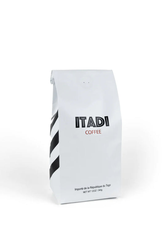 The white Itadi Coffee bag from sonia's-vokalized-kreations features a minimalist design with bold black stripes and text, emphasizing its earthy flavor. Made from beans sourced from family-owned farms, it promises both quality and tradition in every sip.