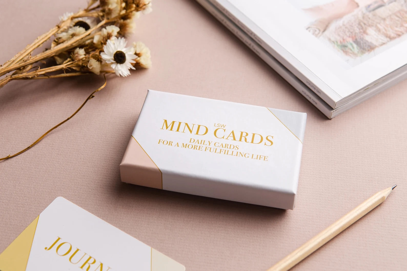 A box of "Mind Cards: Daily Cards" by sonia's-vokalized-kreations rests on a table with a journal, pencil, dried flowers, and a book. These cards nurture positive habits and boost mental health with daily inspiration.