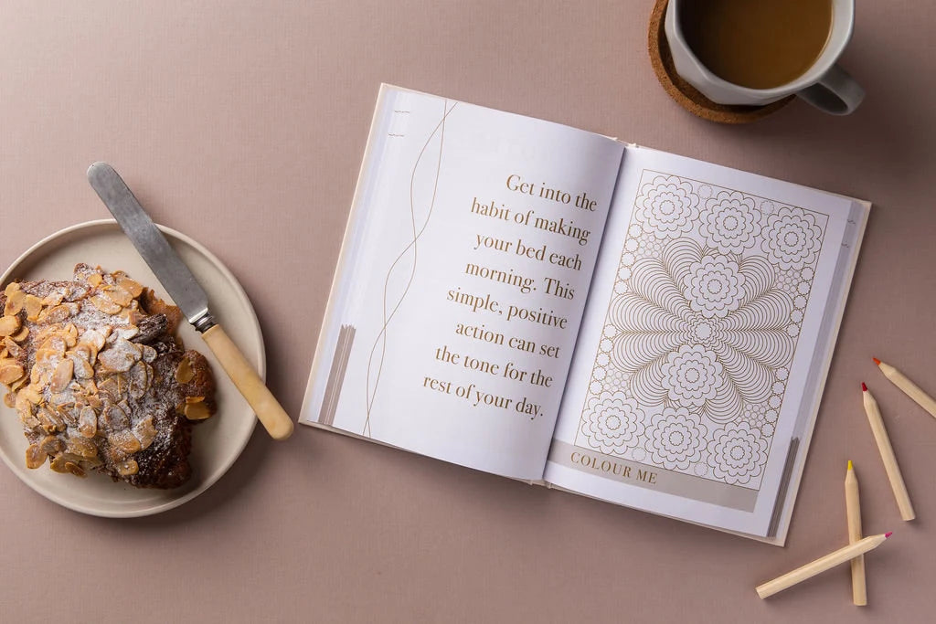 The "Morning Notes Journal" by sonia's-vokalized-kreations features an open book with a motivational quote on making the bed and a coloring mandala for positivity. Nearby, a cozy setup includes a pastry plate, knife, coffee cup, and colored pencils on beige—a daily invitation to well-being.