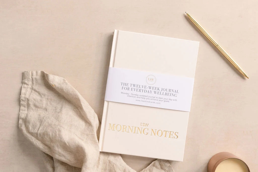 A sonia's-vokalized-kreations Morning Notes Journal rests on a beige surface with a gold pen, soft cloth, and candle, creating the perfect daily well-being journal to cultivate healthy habits and foster a positive mindset.