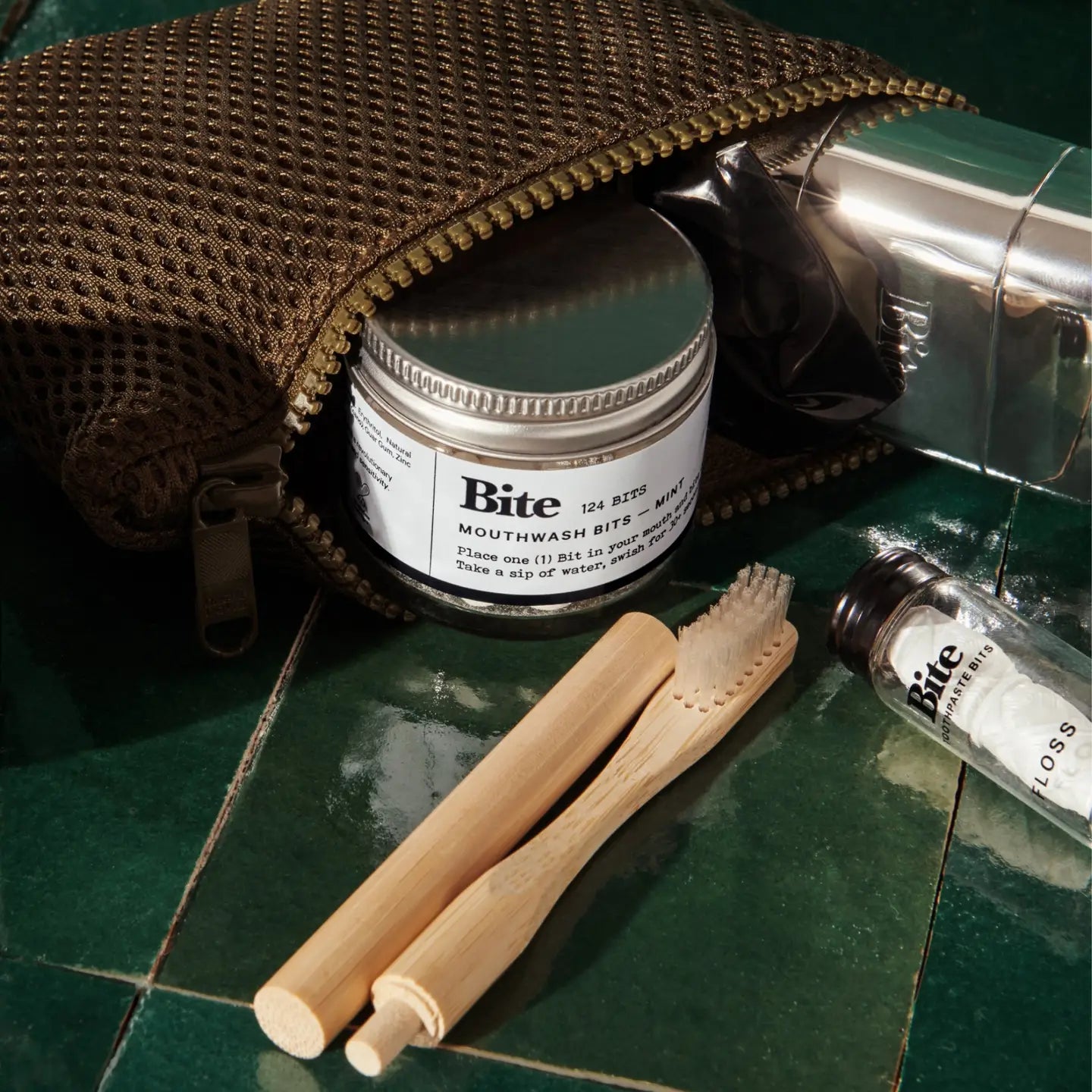 Bite mouthwash bits container with toothbrushes and a pouch on a green surface