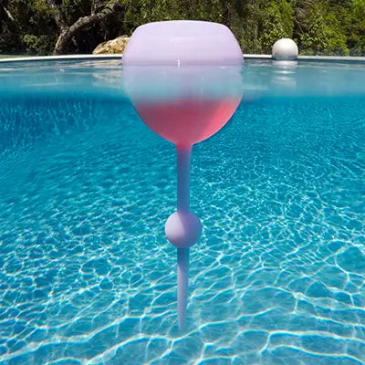 The Sonia's Vokalized Kreations Floating Wine Glass for Beach, Pool & Outdoors – Reusable Acrylic – stays upright in the pool, partially submerged as the waterline cuts through the durable drinkware.