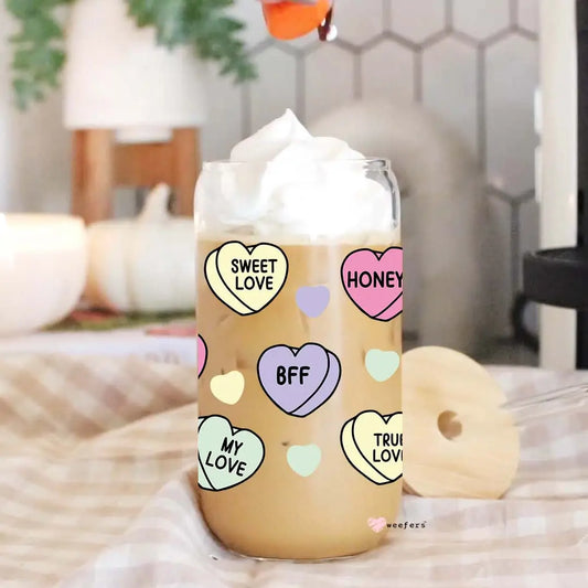 Iced coffee in a Sonia's Vokalized Kreations Libbey glass cup with whipped cream, featuring a bamboo lid, bent straw, and colorful hearts with "SWEET LOVE," "HONEY," and "BFF" designs.