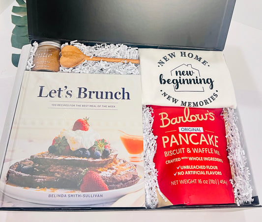 The Let's Brunch Kitchen Housewarming Gift Box by Sonia's Vokalized Kreations includes the "Let's Brunch" cookbook, wooden spoon, breakfast blend seasoning, Barlow's pancake mix, and a "New Home" tea towel—perfect for cozy mornings.