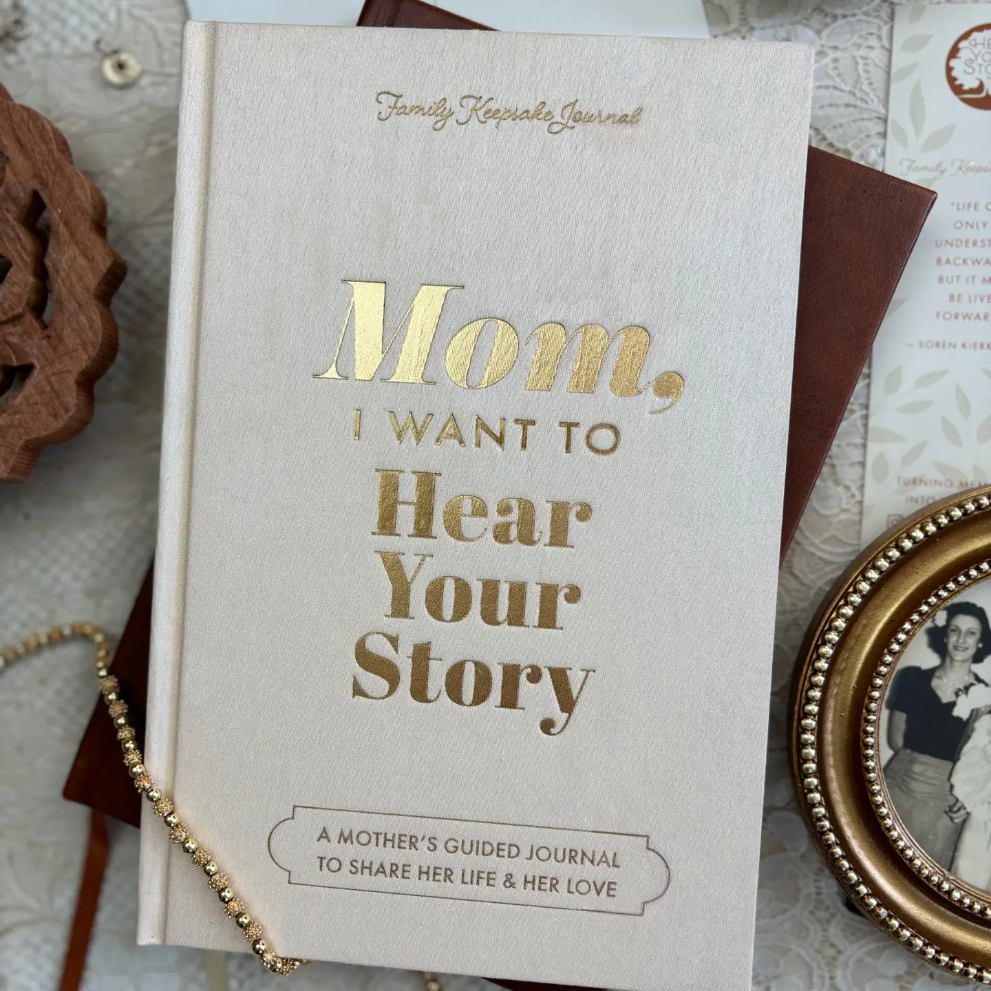 The "Mom, I Want To Hear Your Story; Heirloom Edition" journal by Sonia's Vokalized Kreations rests on lace beside keepsakes—a thoughtful gift for mothers to record and share memories with loved ones.